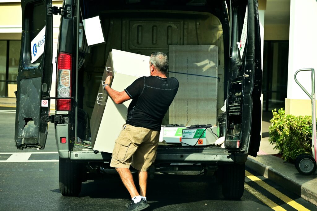 Adult man loading furniture into an open van in a parking lot, daytime setting.