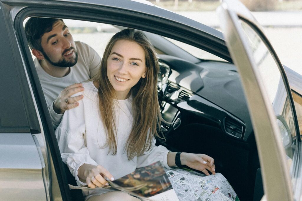 Smiling couple inside a car with map, ready for an adventurous road trip.