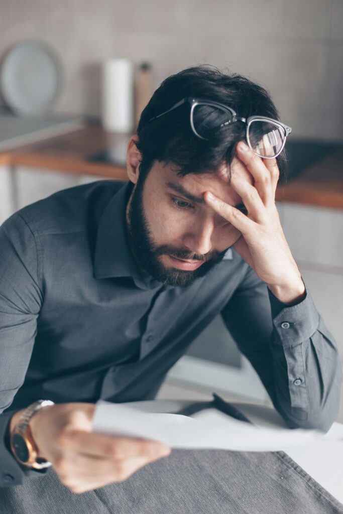 Man with eyeglasses on head looks worried as he reads paperwork, expressing concern.