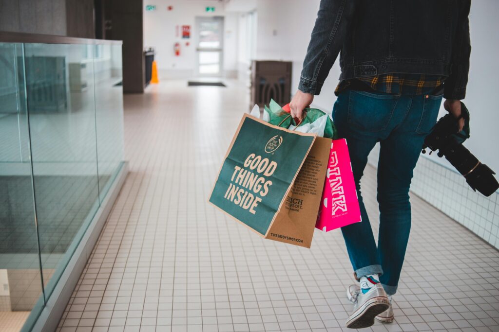 Casually dressed man carrying shopping bags and camera indoors at mall.