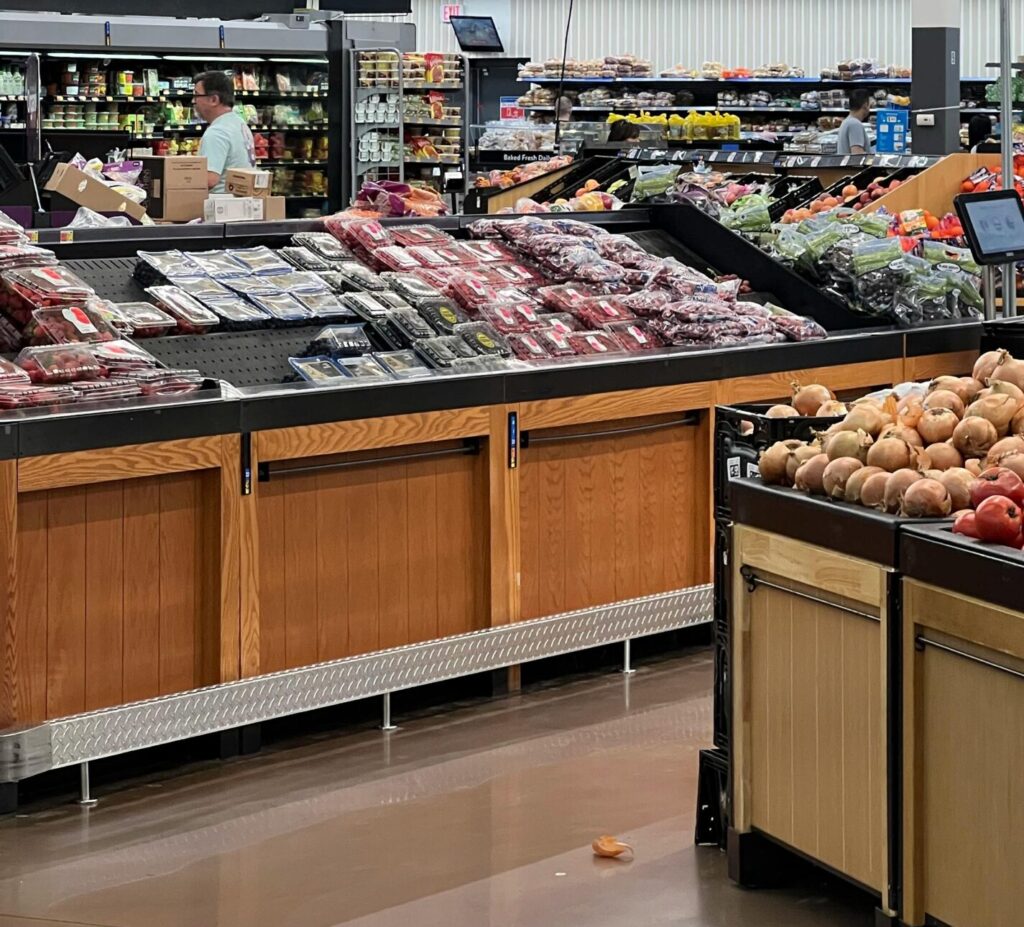 Modern grocery store produce section with fresh fruits and bakery signs.